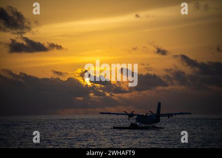 Ein faszinierender Sonnenuntergang über den blauen Malediven, mit einem Wasserflugzeug, das über das türkisfarbene Meer gleitet, schafft eine idyllische und ruhige Insel Stockfoto