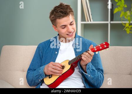 Attraktiver junger Mann, der auf der sofa.interior Ukulele spielt Stockfoto