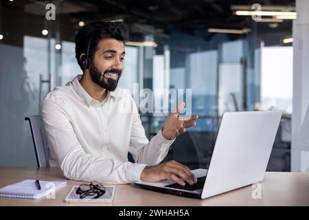 Junger indischer Unternehmer, der aktiv an einer Videokonferenz in einem modernen Büroumfeld teilnimmt und Professionalität zum Ausdruck bringt. Stockfoto