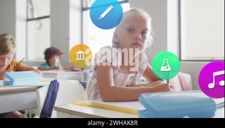 Bild von Schulikonen über lächelndem weißem Schulmädchen, das im Unterricht am Schreibtisch arbeitet Stockfoto