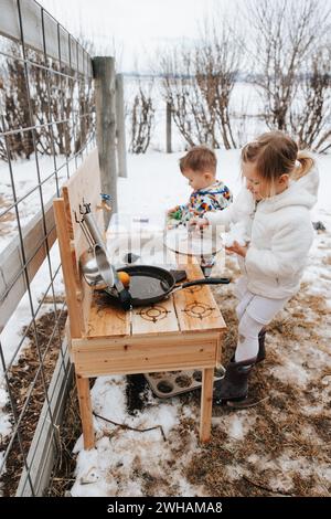 Geschwister spielen in der verschneiten Schlammküche, Winterspaß Stockfoto