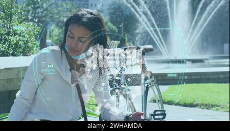 Bild der covid-19-Zelle und des Oszilloskops über Frau mit Gesichtsmaske mit Smartphone Stockfoto