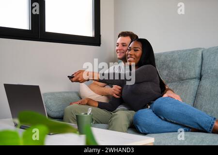 Ein multiethnisches Paar, das zu Hause auf einem Sofa sitzt. Stockfoto