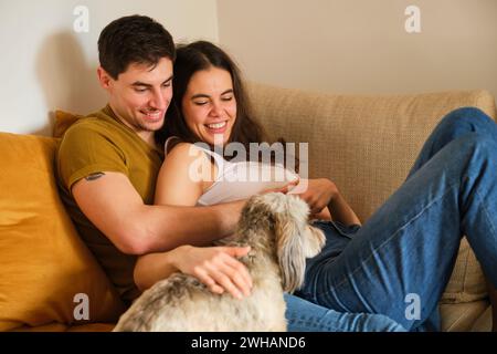 Spanisches lächelndes Paar verliebt auf dem Sofa mit ihrem Hund. Stockfoto