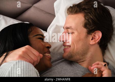Ein verliebtes multirassisches Paar, das sich umschließt und auf dem Bett liegt. Stockfoto