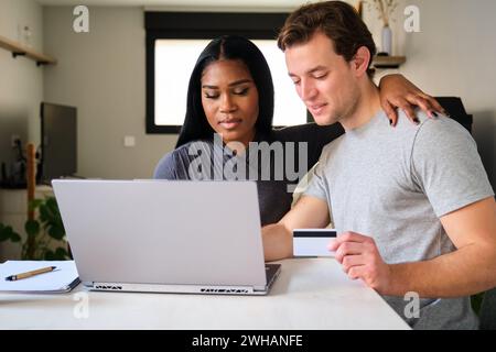 Multiethnische Paare, die online mit Laptop und Kreditkarte einkaufen. Stockfoto
