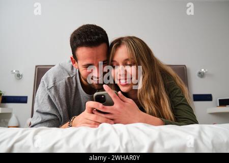 Spanisches glückliches junges Paar, das das Telefon zusammen im Bett benutzt. Stockfoto