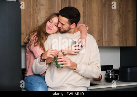 Das junge spanische Paar umarmt sich verliebt, während es einen Kaffee in der Küche trinkt. Stockfoto