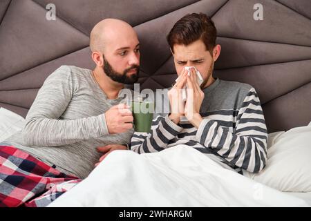 Ein Mann, der sich die Nase in ein Taschentuch bläst, während sein Freund sich um ihn kümmert. Stockfoto