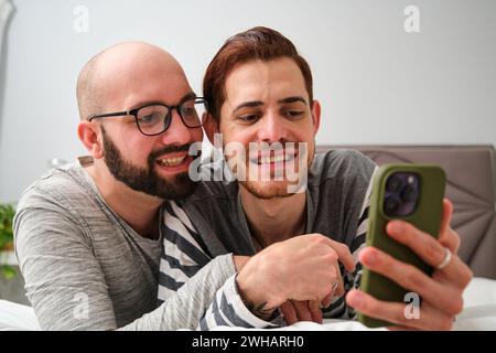 Homosexuelles glückliches Paar, das das Telefon zusammen im Bett benutzt. Stockfoto