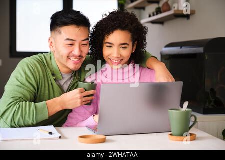 Multirassisches glückliches Paar, das den Laptop benutzt und Kaffee trinkt. Stockfoto