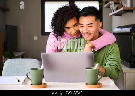 Multirassisches Paar lächelt mit dem Laptop und umarmt sich. Stockfoto