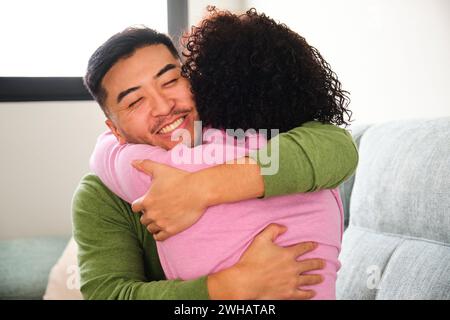 Ein chinesischer Mann umarmt seine dominikanische Freundin zu Hause. Stockfoto