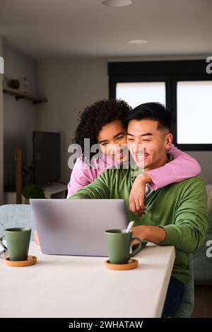 Multiethnisches Paar lächelt mit dem Laptop und umgeht es. Stockfoto