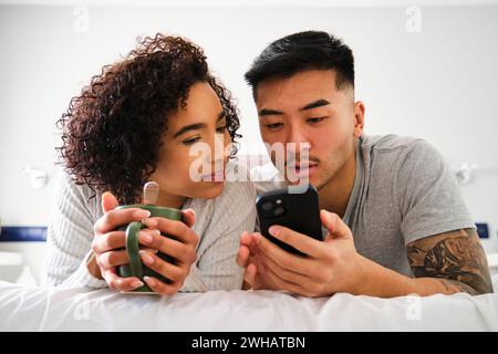 Multiethnisches Paar mit Smartphone im Bett. Stockfoto