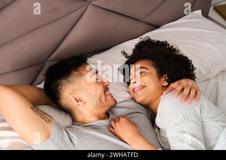 Multiethnisches glückliches Paar, das sich mit Liebe im Bett sieht. Stockfoto