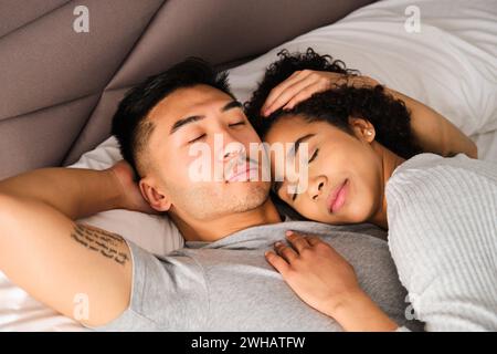 Multiethnisches glückliches Paar, das umarmt auf dem Bett schläft. Stockfoto