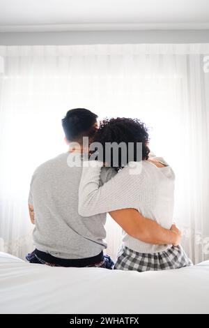 Multirassisches romantisches Paar, das sich umarmt, im Bett mit Hintergrundbeleuchtung zu sitzen. Stockfoto
