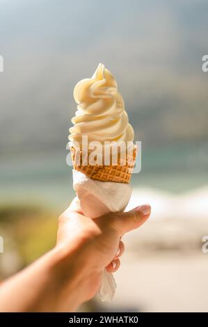 Hand hält Vanilleeis in einem Kegel vor dem Hintergrund des Strandes Stockfoto