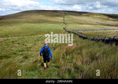 Lone man (Wanderer) Walking on Path by the Wall vom „Harland Hill“ zur „Height of Hazely“ in der Nähe von West Burton im Yorkshire Dales National Park, England. Stockfoto