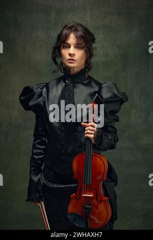 Porträt eines Geigers in viktorianischem schwarzem Kleid, der eine Geige vor dunklem Vintage-Hintergrund hält. Poster für das Festival der klassischen Musik Stockfoto