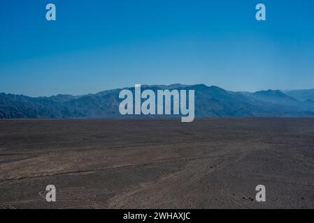 Blauer Himmel und braune Wüste im felsigen Hochland bei Nazca mit Wüstenpflanzen und wenig Wasser in Nazca Peru Stockfoto