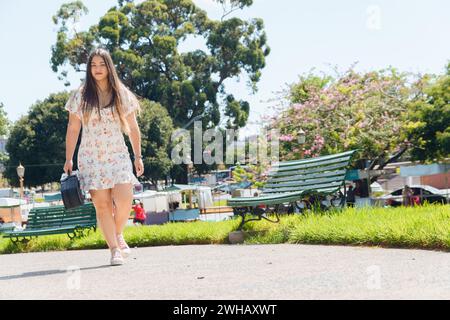 Die junge lateinerin trägt ein weißes Kleid, die im Quadrat mit einem Geigenkasten läuft, um Musik auf der Straße zu machen, im Kopierraum Stockfoto