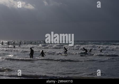 Wassersportbegeisterte mit verschiedenen Formen des Surfens und Segelns in Schwarzweiß in der Abenddämmerung fotografiert am Strand von Beit Yanai, Israel Beit Yanai Stockfoto