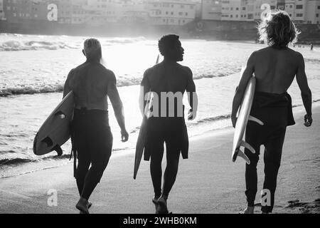 Surfer-Männer mit mehreren Generationen, die vor der Surfsession am Strand spazieren gehen - multirassische Menschen, Lifestyle und Sportkonzept - konzentrieren sich auf Center afri Stockfoto