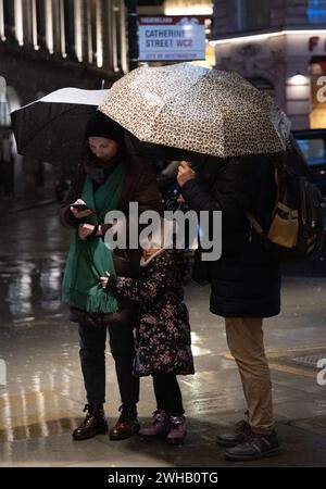 Touristen mit Regenschirmen an einer verregneten Winternacht in Aldwych, Londons Theaterviertel im West End, London, England, Großbritannien Stockfoto