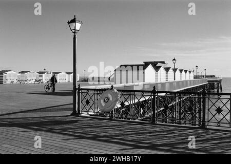 Hastings Pier, East Sussex, UK, in Schwarzweiß, mit Strandhütten, bei Sonnenschein Stockfoto