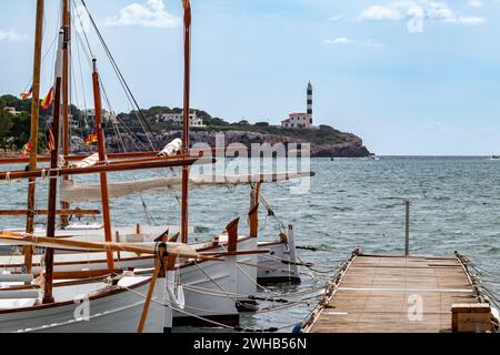 Portocolom, Mallorca, Balearen, Spanien, Szene mit festgemachten traditionellen mallorquinischen Fischerbooten namens Llagut und Portocolom Leuchtturm Stockfoto