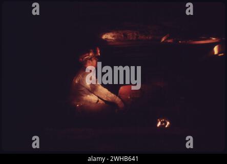 Richlands, Virginia, USA. April 1974. Ein Bergmann, der im Glühen einer Lampe eines Kollegen gebadet ist, wird mit einem Rolltor gezeigt, der für den Transport von Sicherheitsmännern oder anderen kleinen Gruppen verwendet wird. Die Shuttles, die für die Bergleute zum und von der Arbeit genutzt werden, sind größer. Dies ist die Virginia-Pocahontas Coal Company Mine Nr. 3 in der Nähe von Richlands, Virginia Stockfoto