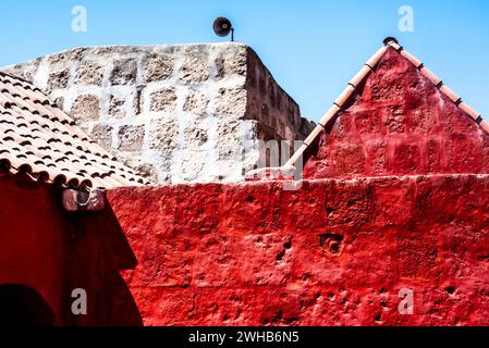 Haus mit roter Wand und braunem Ziegeldach mit Steinmauer und blauem Himmel in Cuzco Inca Stadt in Peru Stockfoto