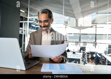 Glücklicher Geschäftsmann mittleren Alters, der sich mit einem Notebook-Hybrid beschäftigt, der im Büro arbeitet. Stockfoto