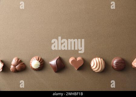 Eine Auswahl an Bonbons aus dunkler Schokolade und Milchschokolade auf braunem, strukturiertem Hintergrund, die in einer Reihe angeordnet sind. Draufsicht. Stockfoto