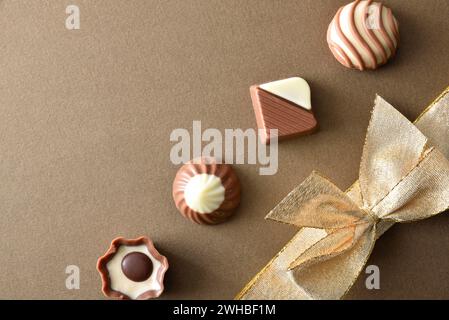 Reihe von verschiedenen schwarzen und weißen Milchschokolade-Pralinen schräg auf braun strukturiertem Hintergrund mit goldener Schleife. Draufsicht. Stockfoto