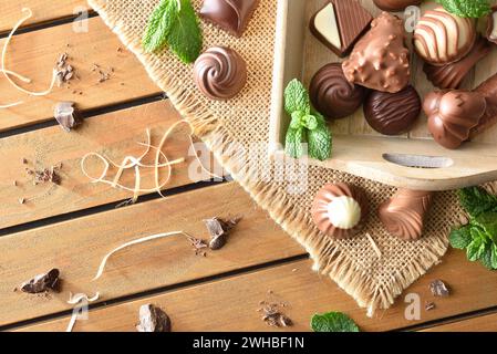 Verschiedene dunkle und Milchschokoladen aus biologischem Anbau auf Holztablett auf Sackleinen auf Holztisch mit Minzblättern und Schokoladenstücken draußen Stockfoto