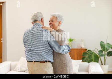 Bleiben Sie in Bewegung. Ein romantisches älteres Ehepaar, das zu Hause zu Musik tanzt. Glückliche lächelnde Familie pensionierter Mann Frau Ehemann Frau, die Spaß hat, die Zeit zusammen zu genießen. Familie Moment Liebe Pflege Stockfoto