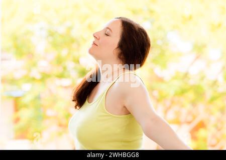 Aufnahme eines Seitenporträts einer glücklichen Frau, die draußen frische Luft in einem natürlichen Hintergrund atmet Stockfoto