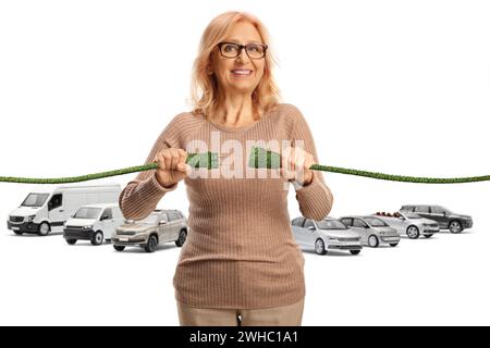 Frau mittleren Alters, die grüne Elektrokabel vor Fahrzeugen auf weißem Hintergrund einschließt Stockfoto