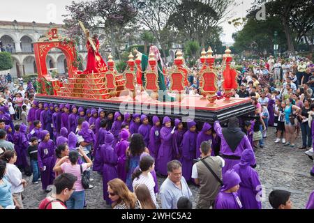 Antigua, Guatemala. Zuschauer, Familien und Touristen beobachten Jugendliche Jungen, die während der Karwoche in La Semana San in einer religiösen Prozession einen Schwimmer tragen Stockfoto