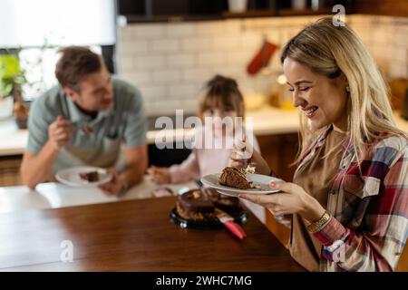 Eine herzerwärmende Szene entfaltet sich, während eine Familie einen köstlichen Schokoladenkuchen zusammen in der Wärme ihrer sonnendurchfluteten Küche genießt und Lächeln und cr teilt Stockfoto