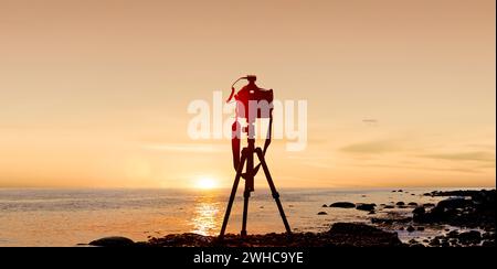 Fotokamera mit Stativ vor einem Sonnenuntergang am Meer Stockfoto