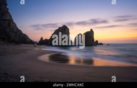 Epic Ursa Beach mit Rock Silhouette und Reflexion gegen goldenen Sonnenuntergang Licht. Cabo da Roca, Sintra an der Atlantikküste in Portugal. Stockfoto