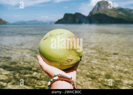 Kokosnuss in männlichen Händen gegen exotische Ozeaninseln. Stockfoto