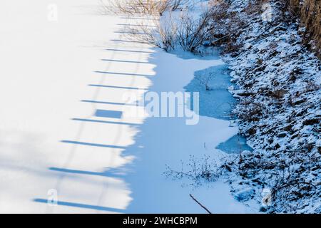 Schatten von hölzernen Zaunpfosten auf der weißen Oberfläche des gefrorenen Sees in der Nähe der Küste in Südkorea Stockfoto