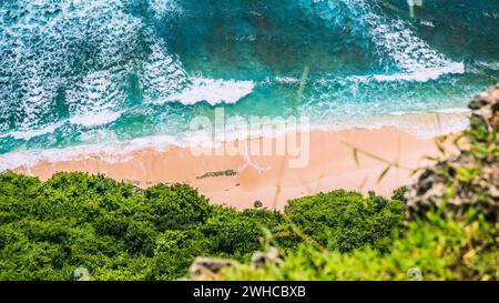 Blick aus der Vogelperspektive auf die rollenden türkisfarbenen Meereswellen über reinem, klarem Sandstrand an sonnigem Tag. Umgeben von üppig grünem Dschungel. Stockfoto