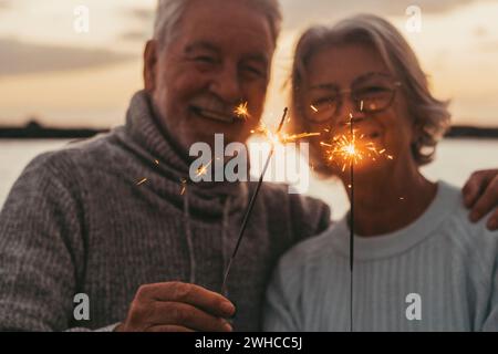 Zwei alte Senioren, die am Abend am Strand glitzernde Lichter halten und Spaß haben Stockfoto