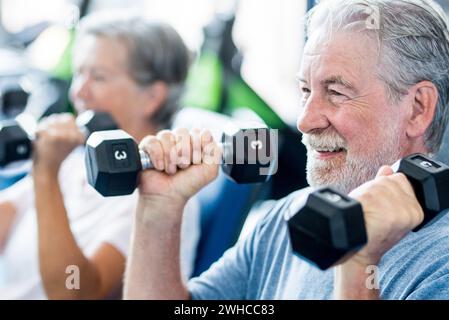 Reifer Mann mit seiner Frau tun Übung Bizeps an Das Fitnessstudio - Fitness und gesundes Lifestyle-Konzept - Training Ihr Körper zusammen - ein Paar von zwei Senioren Stockfoto